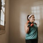 Senior woman in a brightly lit room exercises with dumbbells, promoting fitness at home.